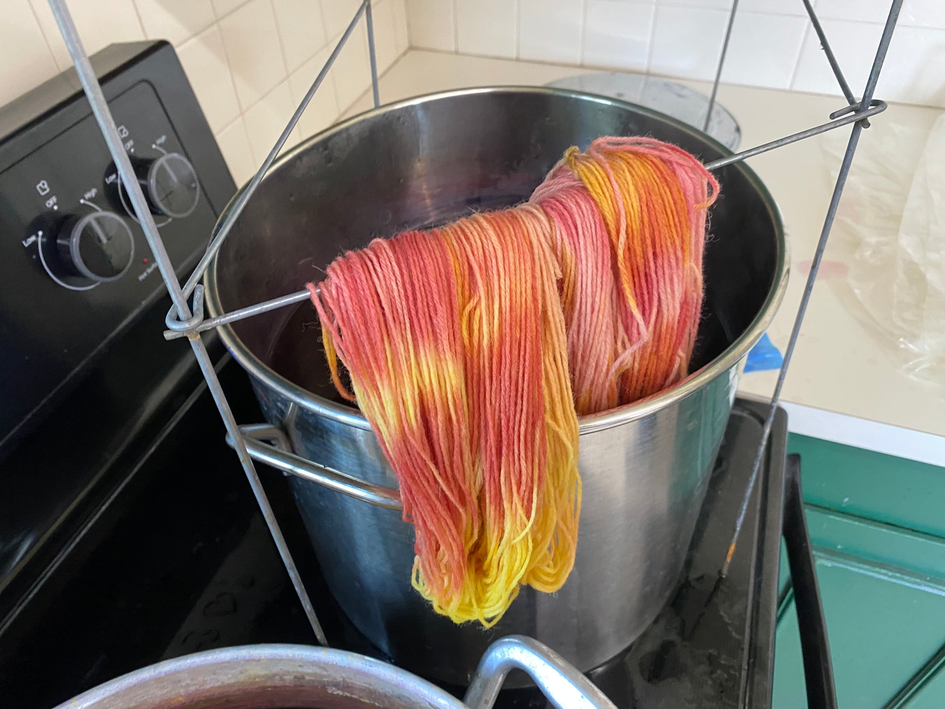 Orange and Yellow Yarn on the Dip bar over a dye pot on the stovetop.. 